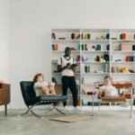 "Psicólogo infantil avaliando duas crianças em um ambiente terapêutico moderno. A sala possui uma estante com livros organizados, criando um espaço acolhedor para sessões de terapia, psicopedagogia ou avaliação do desenvolvimento infantil. O profissional observa atentamente enquanto as crianças demonstram diferentes expressões e posturas. Imagem ideal para temas sobre autismo, TDAH, terapia infantil e desenvolvimento cognitivo."